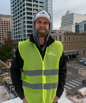 Man in a high-visibility safety vest standing on a rooftop, emphasizing Cool Roofs' roofing inspection services.