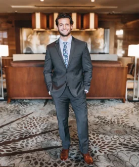 Man in a suit standing confidently in a modern interior, promoting professionalism and expertise relevant to roofing services.