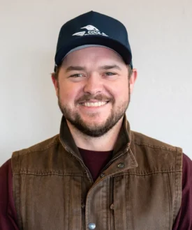 Smiling man wearing a Cool Roofs cap and a brown vest, representing Cool Roofs roofing services focused on hail damage inspections and repairs.