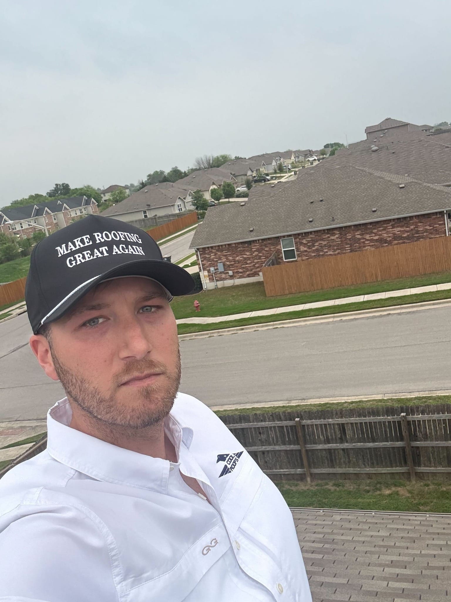 Man on a roof wearing a "Make Roofing Great Again" cap, showcasing residential neighborhoods in San Antonio, emphasizing expertise in roofing services.