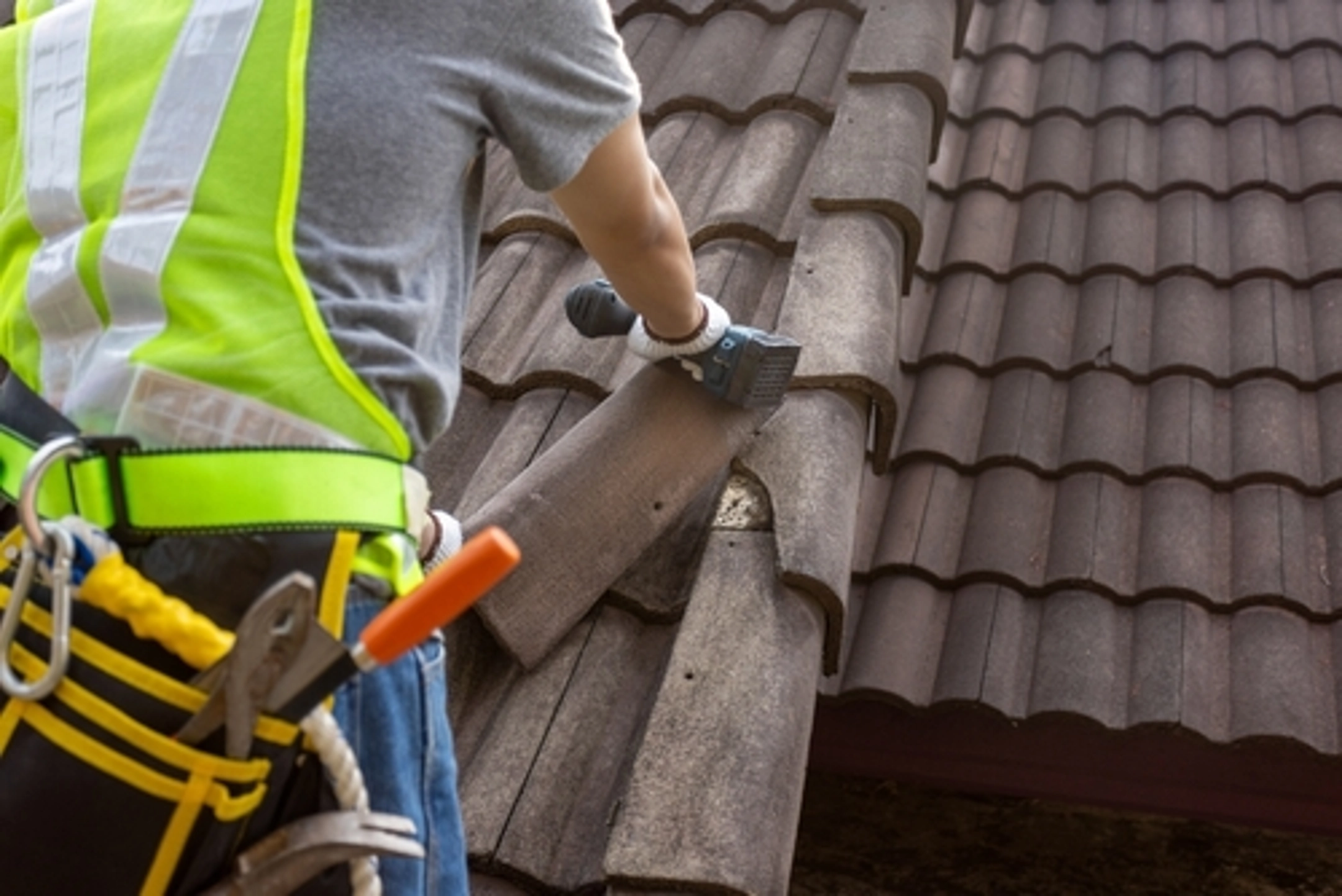 Roofing contractor repairing shingles on a residential roof, wearing safety gear and using a power tool, emphasizing Cool Roofs Inc.'s roofing services.