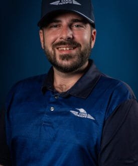 Man wearing a blue polo shirt and cap with Cool Roofs logo, smiling against a blue background, representing roofing services expertise.