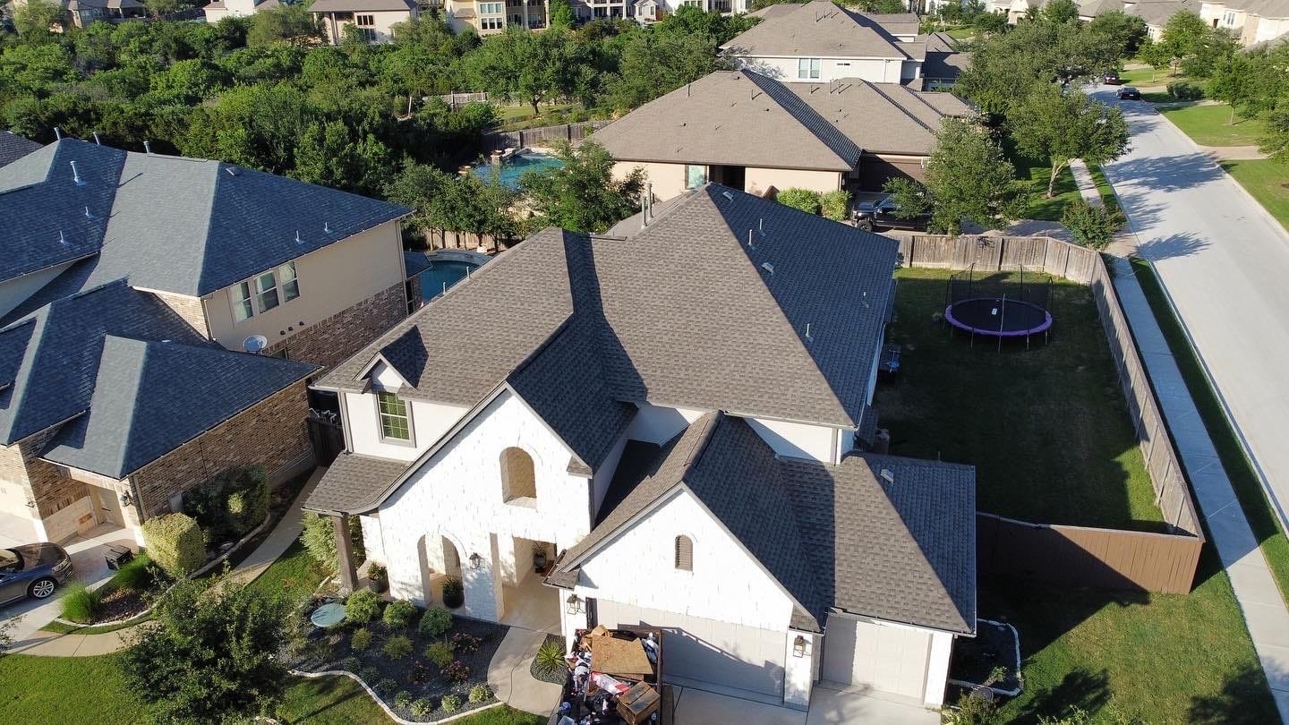Residential roofing installation with gray shingles on a modern house, surrounded by greenery and a trampoline in the backyard, highlighting roofing solutions for church buildings by Cool Roofs.