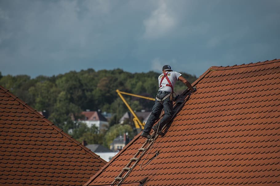 Roofer working on a steep, red-tiled roof, demonstrating roofing services and expertise related to storm damage repairs and roof replacements in New Jersey.