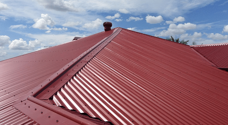 Red metal roofing installation with prominent ridges and ventilation cap under a bright blue sky, showcasing durable and energy-efficient commercial roofing solutions.