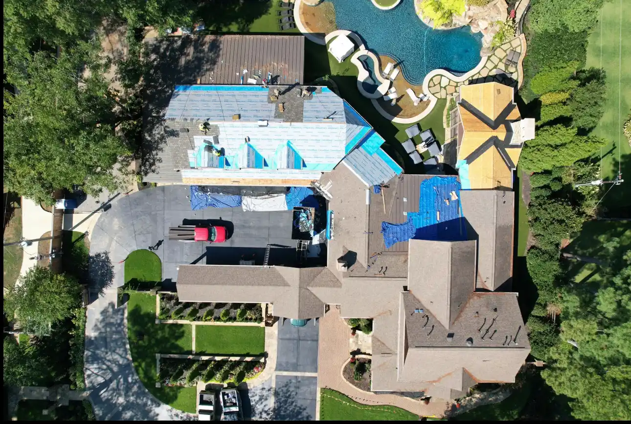 Aerial view of a residential property with ongoing roof installation, featuring workers on a partially covered roof, blue tarps, and surrounding landscaping, highlighting CoolRoofs' Homeowners Protection Program.