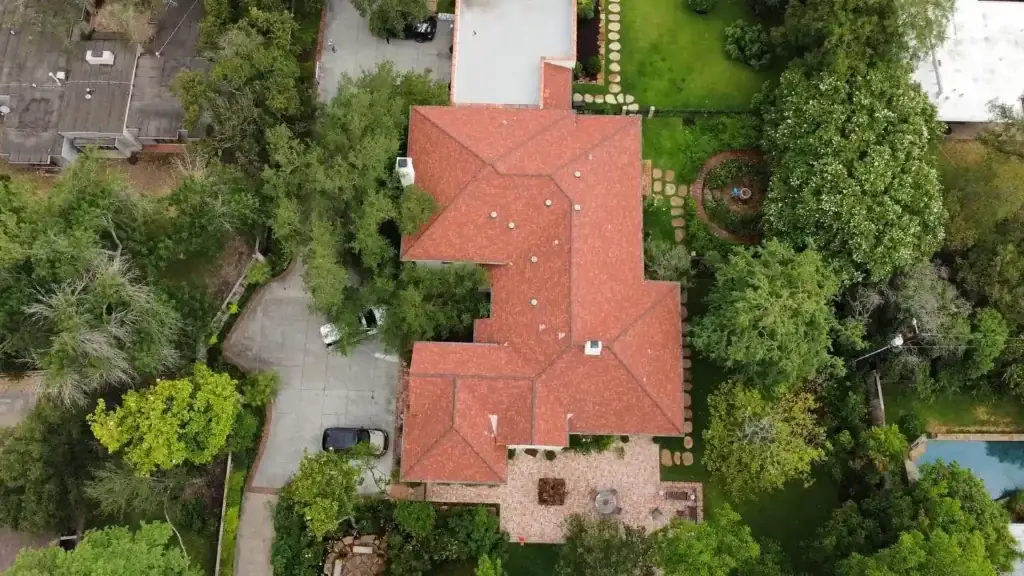 Aerial view of a home with a newly installed red tile roof and surrounding lush landscaping.