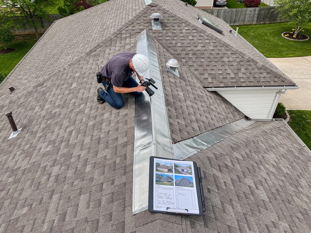 Roofer inspecting shingles and flashing during professional roof inspection, assessing deck condition and potential damage.