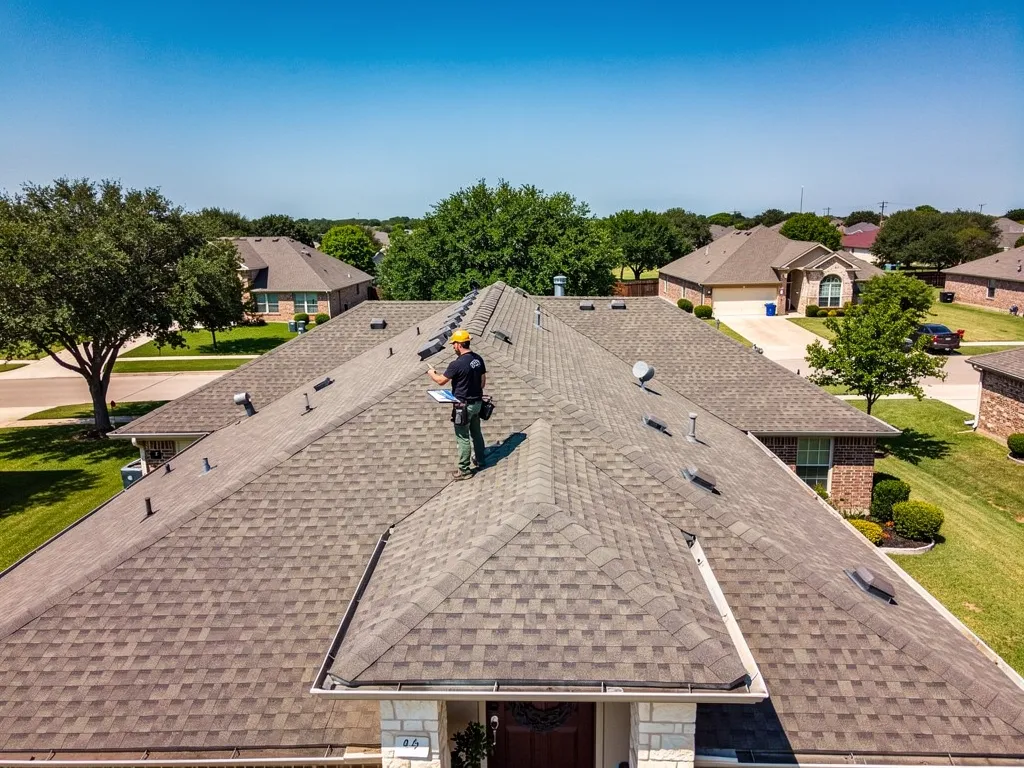 Roofer inspecting residential roof assessing repair versus replacement options in Texas.