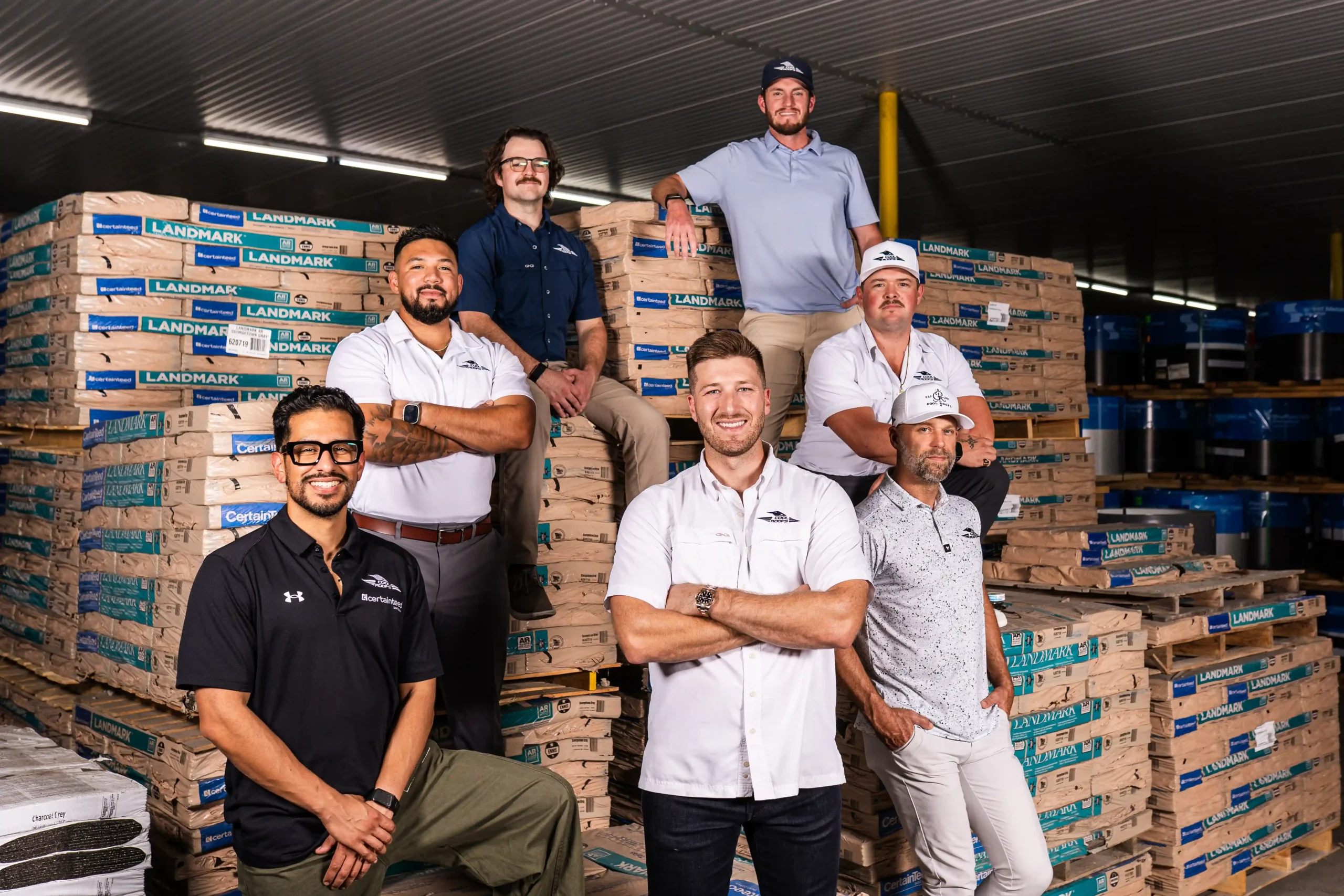 A team of roofing professionals from Cool Roofs, posing confidently in a warehouse stacked with